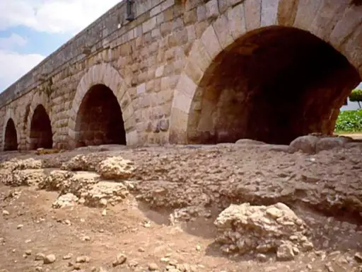 Antiguo puente de piedra con arcos, que es un puente de gran tamaño y robustez, con ruinas a sus pies.