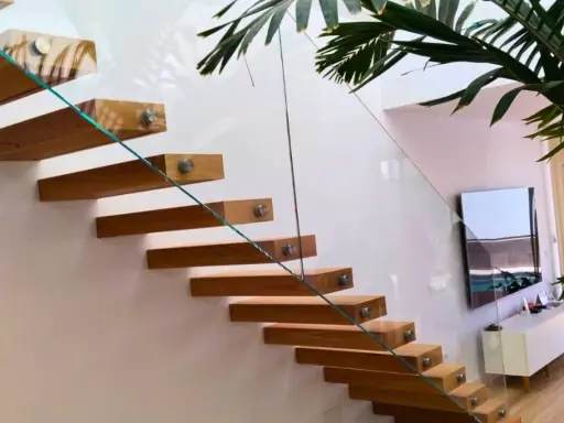 Escalera flotante de madera con **rejas de cristal** que aportan ligereza y modernidad al espacio.