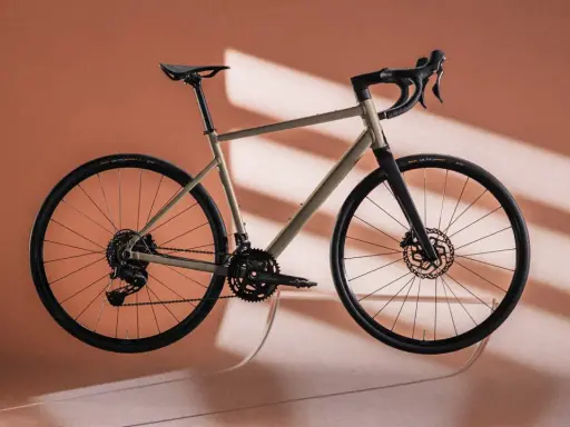 Ein Gravelbike in einem sanften Sandton, das wie ein Kunstwerk schwebt. Der Rahmen und die Reifen bilden einen harmonischen rose blend mit dem Hintergrund.