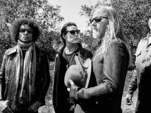 Medlemmar av Alice in Chains, fyra män med solglasögon, står utomhus bland träd. En håller en hatt med fjädrar.