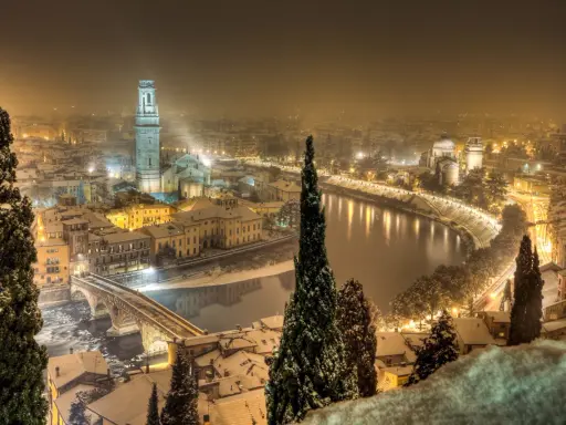 Verona innevata, un'incantevole **città da visitare a dicembre**. La neve copre i tetti e il fiume Adige riflette le luci della città.
