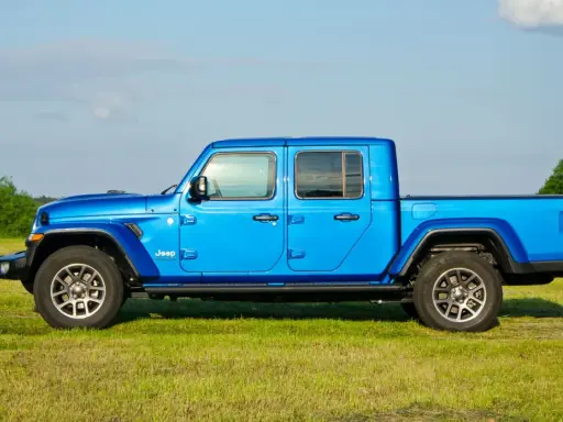Niebieski Jeep Gladiator na tle zielonej łąki i drzew. Ten wszechstronny pickup jest gotowy na każdą przygodę.