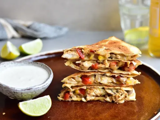 Stos **quesadilli z kurczakiem**, papryką i serem, podane z dipem i limonką.