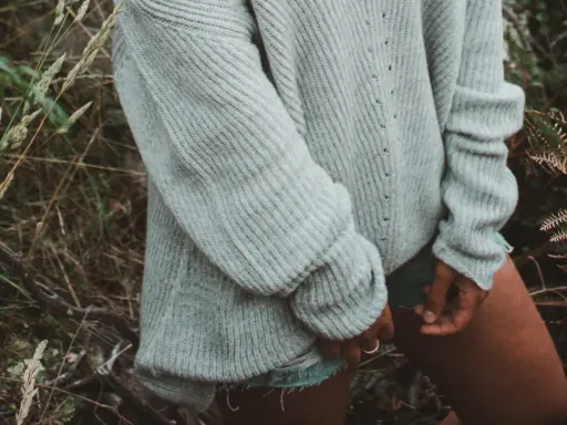 En kvinna i en stickad pullover dam i ljusgrått står i en skog.