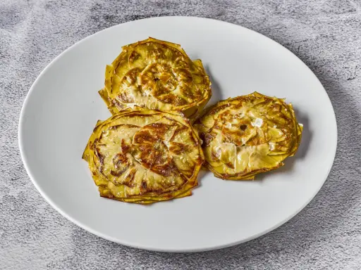 Tres alcachofas cortadas en rodajas, cocinadas a baja temperatura, con un toque de sal marina, servidas en un plato blanco.