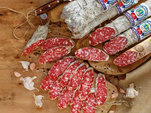 Eine Auswahl an italienischen Salami-Sorten, aufgeschnitten und im Ganzen, mit Knoblauch und Pfefferkörnern auf Holz.