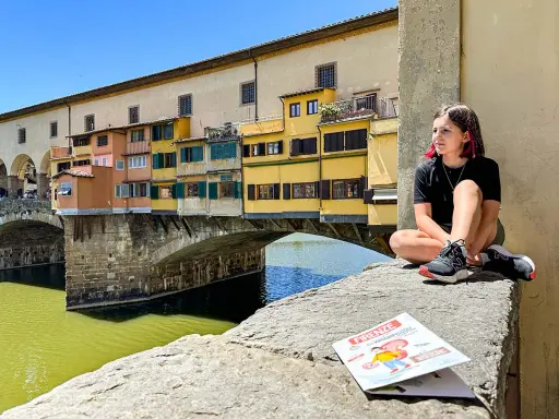 Ragazza seduta sul Ponte Vecchio, con la guida "Firenze cosa vedere in due giorni" a fianco.