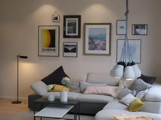 Przytulne mieszkania w Danii: salon z wygodną kanapą, galerią ścienną i designerską lampą.