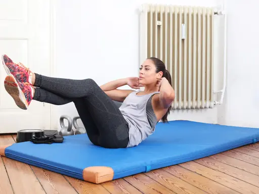 Frau macht Crunches auf einer blauen Matte. Sie trainiert ihren Bauchmuskel, um fit zu bleiben.