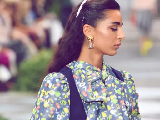 Ein dezenter Haarkamm hält die elegante Frisur einer Frau mit auffälligem Ohrring und geblümtem Kleid im Zaum.