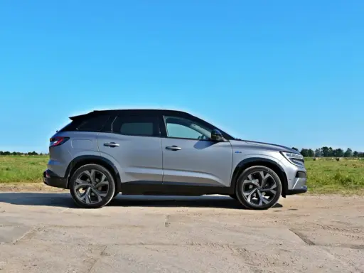 Nowy Renault Austral w kolorze srebrnym, zaparkowany na polnej drodze, z zielonym polem i niebieskim niebem w tle.