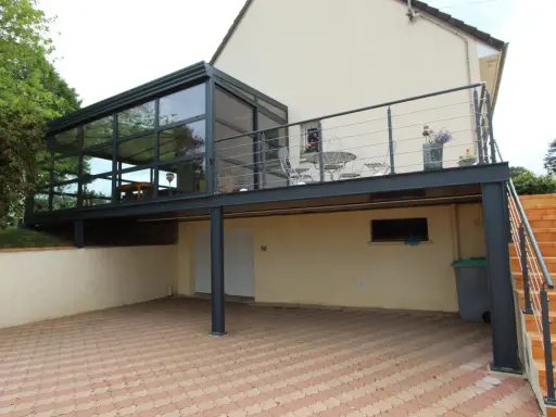 Modèle de véranda sur balcon avec structure métallique et vitrage. Un espace extérieur aménagé avec table et chaises.