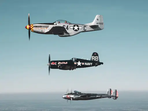 Drei historische Flugzeuge im Flug: eine silberne P-51 Mustang, ein schwarzer Red Bull Flieger (Corsair) und eine P-38 Lightning.