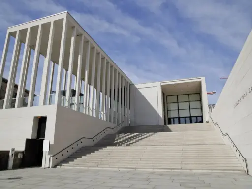 Moderne James-Simon-Galerie mit langer Treppe, ein Werk bekannter Architekten, vor blauem Himmel.