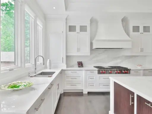 Cocina moderna y luminosa con muebles blancos, encimeras de cuarzo y electrodomésticos de acero inoxidable. Perfecta para pintar muebles de cocina y darles un nuevo aire.