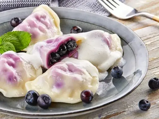 Pyszne pierogi z jagodami, polane śmietaną, z miętą i świeżymi owocami. Idealny przepis na lato!