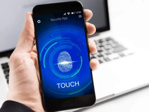 Dłoń trzyma smartfon z ekranem blokady "Security App" i ikoną odcisku palca. Proces autoryzacji jest w toku.