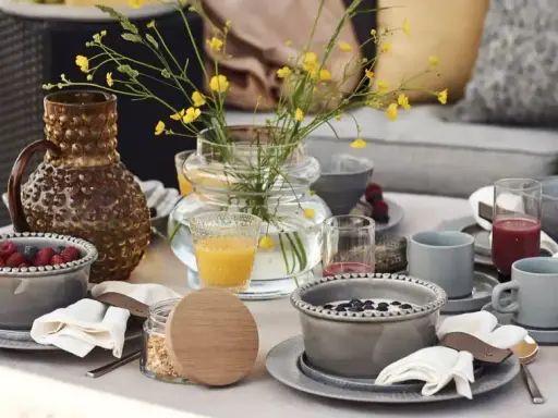 Vacker dukning runt bordet med frukostskålar, bär, juice och en vas med gula blommor.