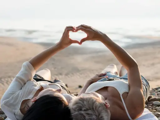 Para, które właśnie wzięło ślub, leży na plaży, tworząc serce dłońmi. Idealne miejsce na podróż poślubną.