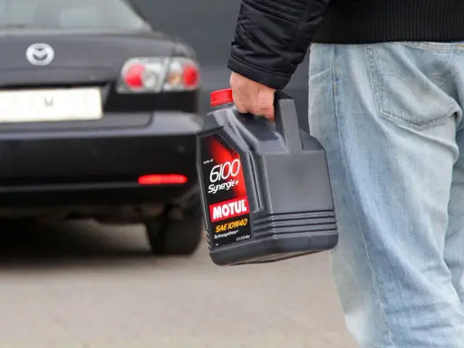 Mężczyzna niesie kanister z olejem silnikowym Motul, gotowy do recyklingu.
