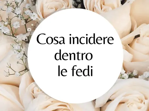 Un cerchio bianco su uno sfondo di rose color crema con la domanda: "Cosa incidere dentro le fedi?". Ispirazione per incisioni fedi nuziali frasi.