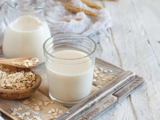 Szklanka i dzbanek z mlekiem owsianym, obok miseczka płatków owsianych. Idealne na zdrowe śniadanie, mleko 2 procent kcal.