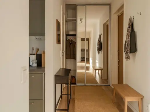 En mysig hall med en lång bänk, en smal konsol och en stor spegelgarderob. En jacka hänger på en krok och en väska med scarf.
