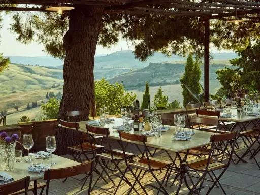 Tavoli apparecchiati sotto un pergolato con vista sulle colline toscane. Un'atmosfera perfetta per gustare i sapori degli agriturismi in Toscana.