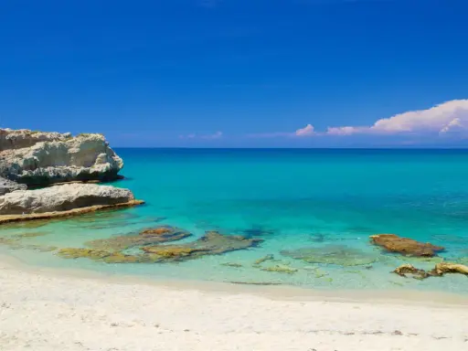Spiaggia di Santa Domenica con rocce bianche e mare cristallino sotto un cielo azzurro.