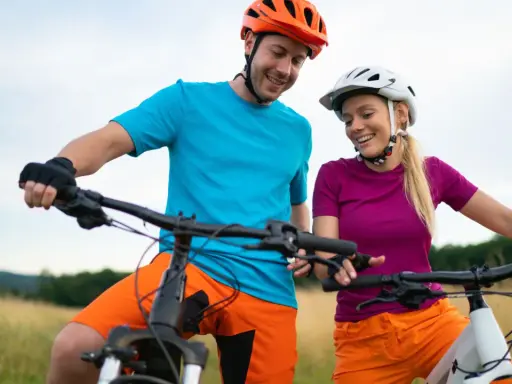 Uśmiechnięta para w kaskach i sportowych strojach, gotowa na przejażdżkę rowerami elektrycznymi. Wygodne akcesoria do roweru elektrycznego zapewniają komfort.