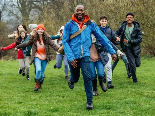Lehrer und Schüler rennen lachend über eine grüne Wiese. Perfekt, um eine Klassenfahrt zu organisieren und Abenteuer zu erleben!