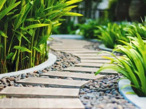 Un moderno camminamento giardino con lastre in pietra e ghiaia, circondato da rigogliosa vegetazione verde.