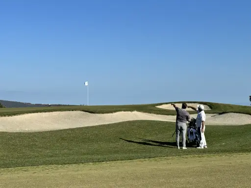 Zwei Golfer planen ihren nächsten Schlag auf dem Valderrama Golfplatz, mit einem Bunker und dem Fahnenmast im Hintergrund.