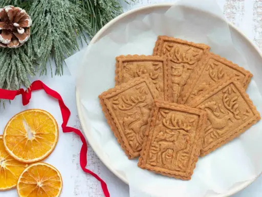 Assiette de sablés rennes de Noël, décorée de branches de sapin givrées, de ruban rouge et de tranches d'orange séchée.