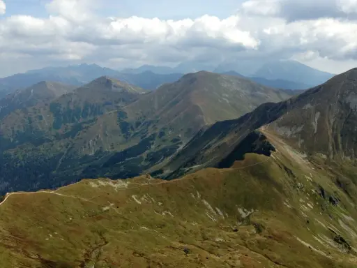 Widok na pasmo górskie, gdzie w Tatry prowadzi wydeptana ścieżka. Chmury na niebie.