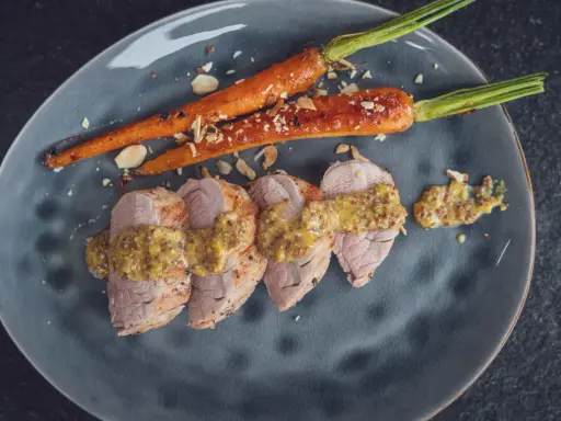 Zarte Scheiben von **schweinefilet grillen** mit Honig-Senf-Sauce und karamellisierten Karotten, bestreut mit Mandelsplittern.