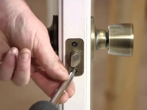 Mano usando un destornillador para desmontar una cerradura de puerta interior, quitando los tornillos de la placa.