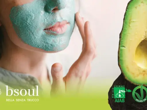 Donna con maschera viso fai da te verde, accanto ad avocado. Certificazioni bio e vegan.