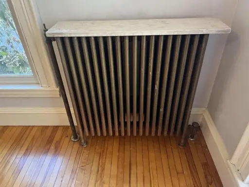 Radiador de latón con tapa de mármol, un ejemplo de calefacción antigua, junto a una ventana.