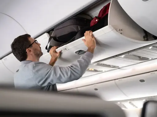Man stänger bagagehyllan med handbagage ombord på ett flygplan från Austrian Airlines.