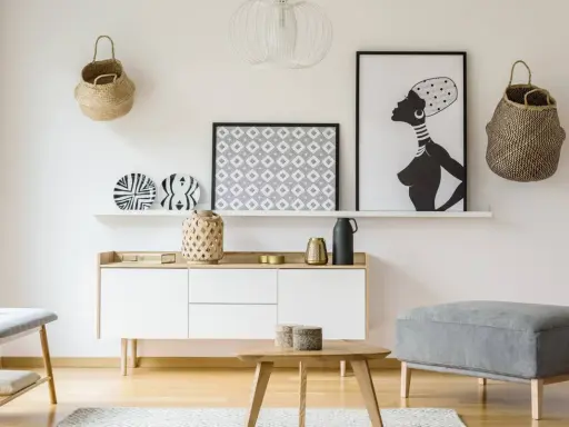 Un mueble blanco resalta sobre una pared clara, complementado con cestas de mimbre y arte africano. El color de pared para muebles blancos es neutro y elegante.