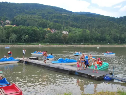 Wakacyjny dzień na Jeziorze Żywieckim. Ludzie pływają na rowerach wodnych, czując się jak na karaibskiej plaży.