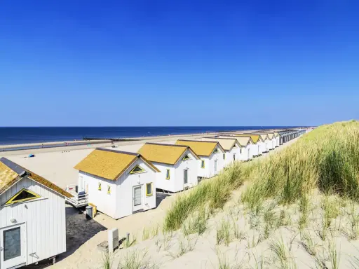Reihen von weißen Strandhäusern mit gelben Dächern am **Holland Strand** unter blauem Himmel.