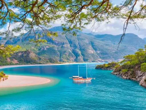 Malownicze widoki na turcja oludeniz: turkusowa woda, piaszczysta plaża i góry. Statek kołysze się na falach.
