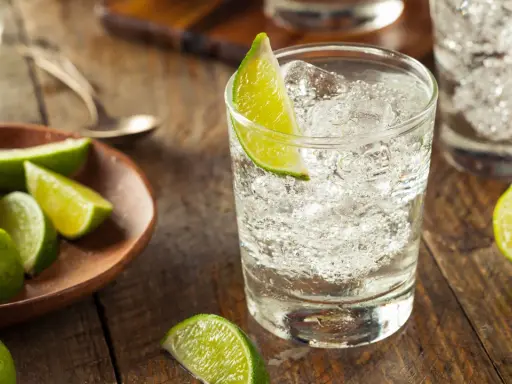 Erfrischender Gin und Bitter Lemon mit Eis und Limettenspalten auf rustikalem Holztisch.