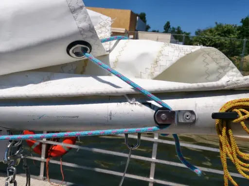 Poulie pour prise de ris automatique sur un mât de bateau, avec des cordages bleus et roses.