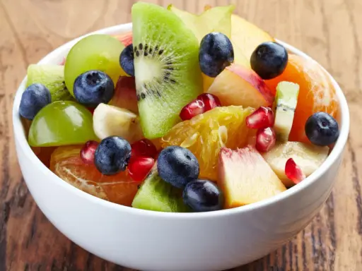 Kolorowa sałatka owocowa zimowa: kiwi, pomarańcza, winogrona, borówki, granat i brzoskwinia w białej misce.