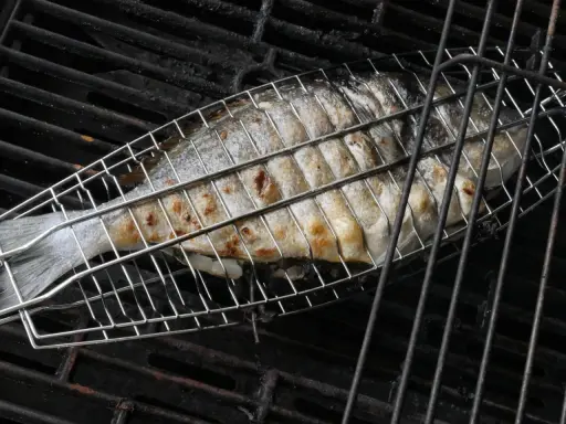 Ein ganzer Fisch wird in einem Grillkorb gegrillt. Die Haut ist goldbraun und leicht gebräunt.