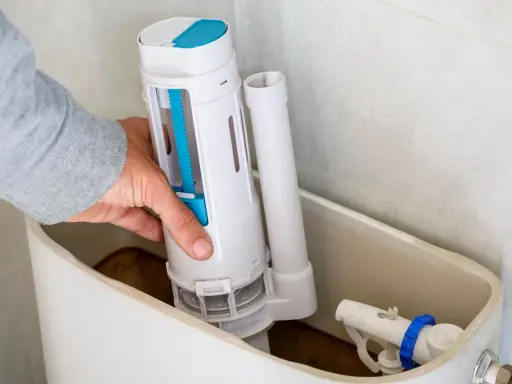 Mano instalando el mecanismo de descarga, una de las partes de una cisterna de baño. Se ve el flotador y la tubería de llenado.