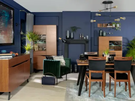 Inspiracje granatowa ściana w salonie: elegancka jadalnia z drewnianymi meblami, aksamitnym fotelem i nowoczesnym oświetleniem.